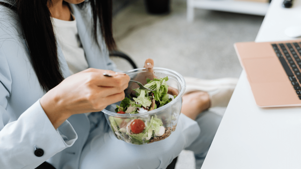 a person eating a salad in front of a laptop