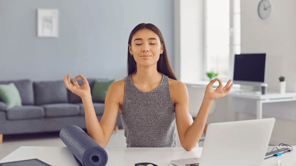 a person meditating on a yoga mat in front of a laptop