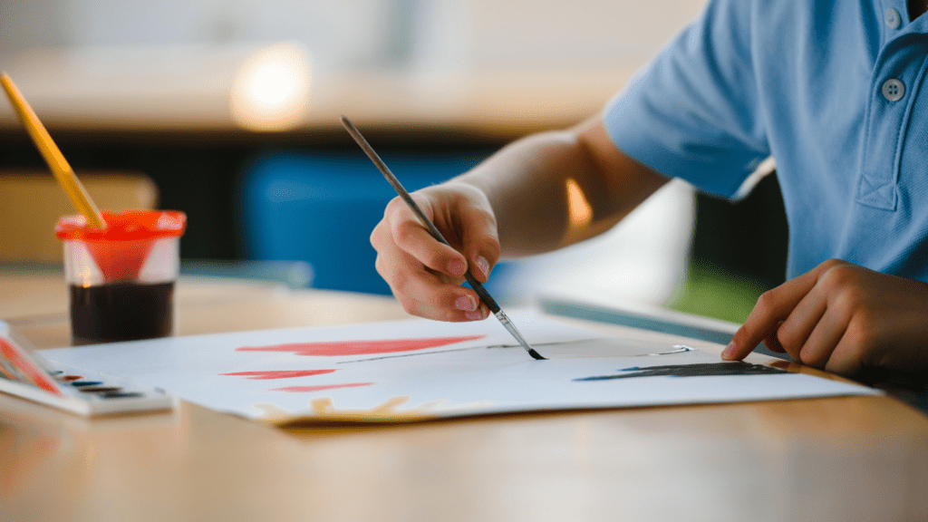 a person sitting at a table with paints and brushes